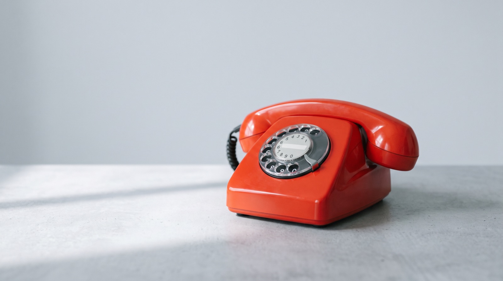 A red rotary telephone on a gray desk against a pale studio backdrop